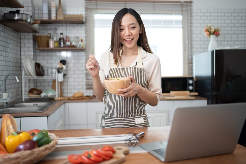 Adorable woman using laptop for recipe while preparing food in kitchen.