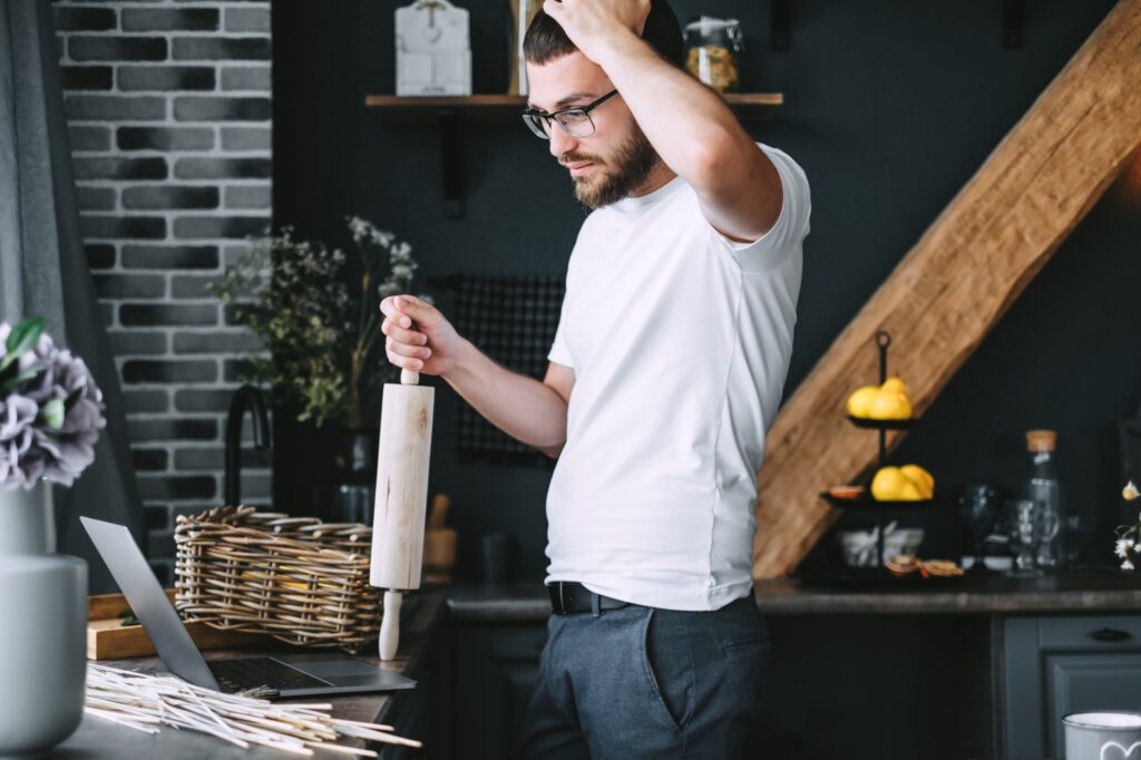 Young pensive caucasian bearded man is looking at food recipes in a laptop